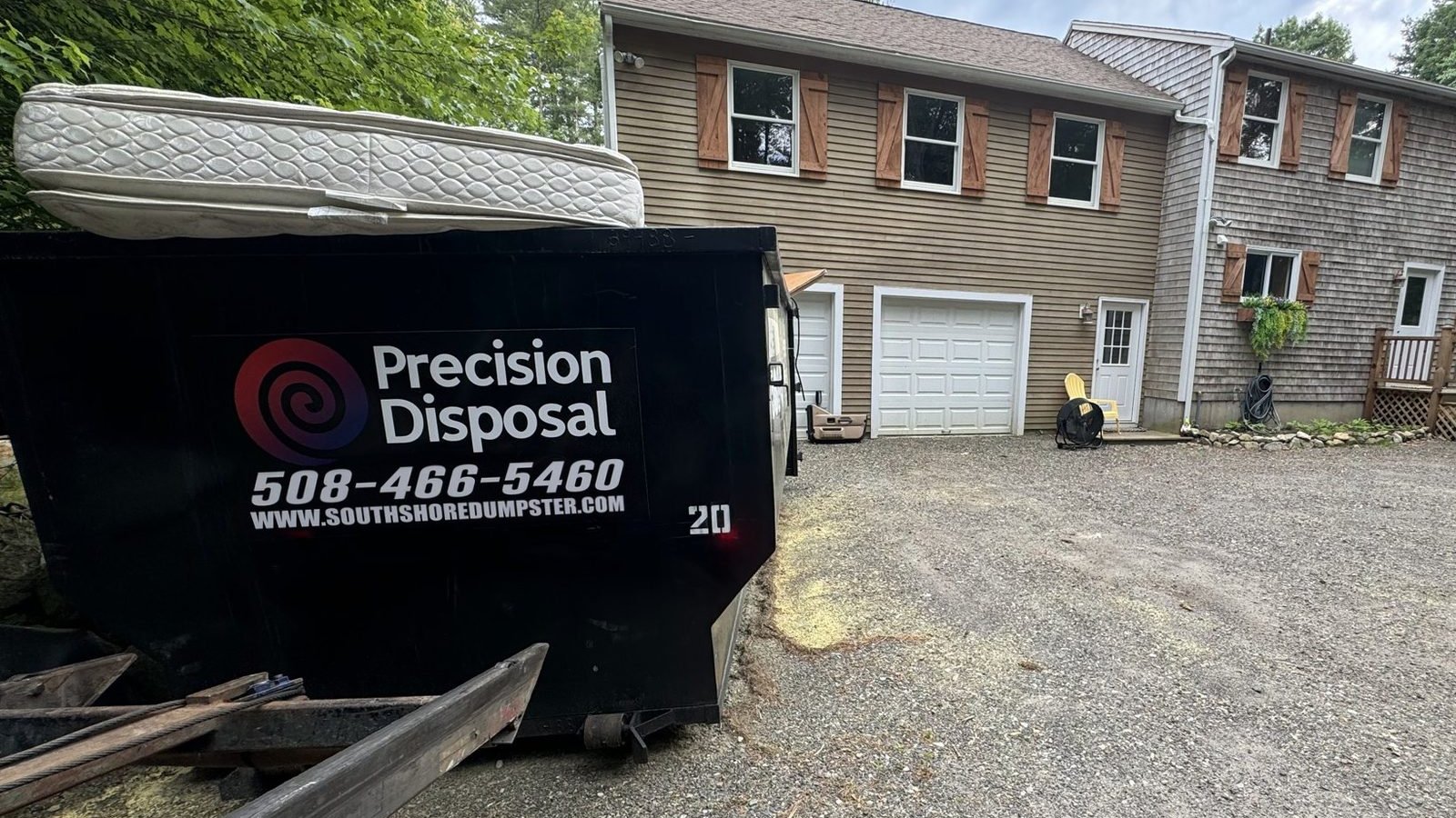 Precision Disposal 20-yard roll-off dumpster with a 508-466-5460 southshoredumpster.com decal and a mattress in a home driveway