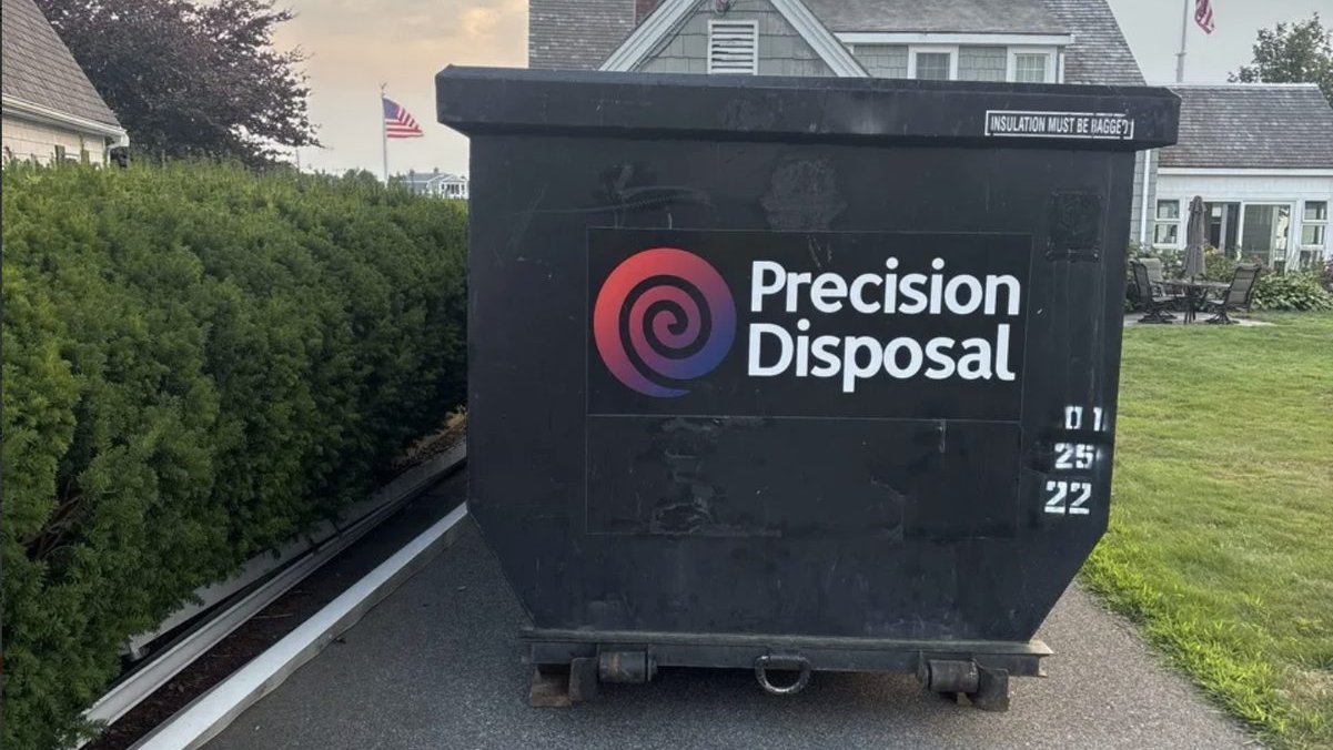 Precision Disposal roll-off dumpster in a residential driveway beside a shingled home