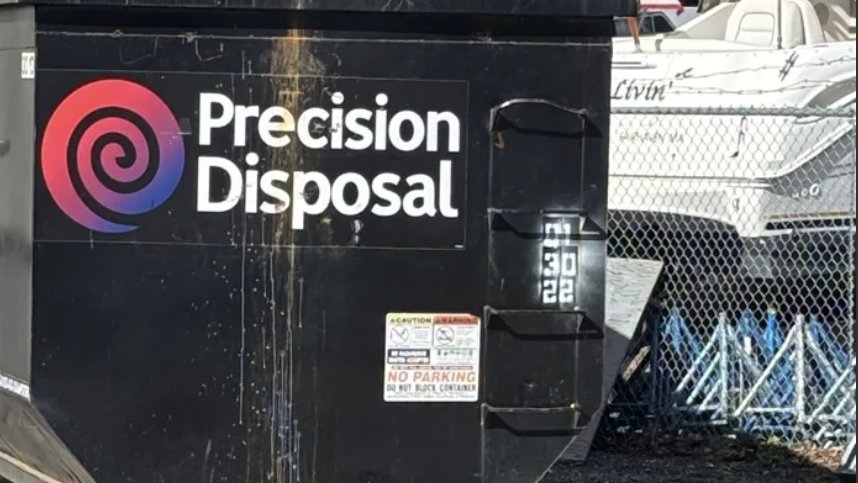 Precision Disposal roll-off dumpster parked beside boats at a boatyard